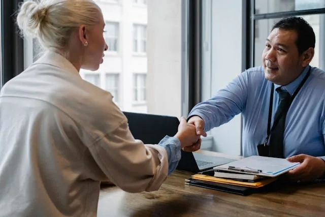 Two people having a business meeting shaking hands over a desk