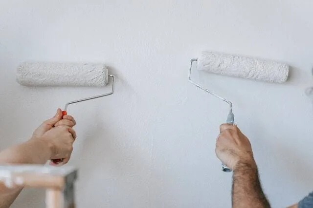 Two people paint a wall with paint rollers